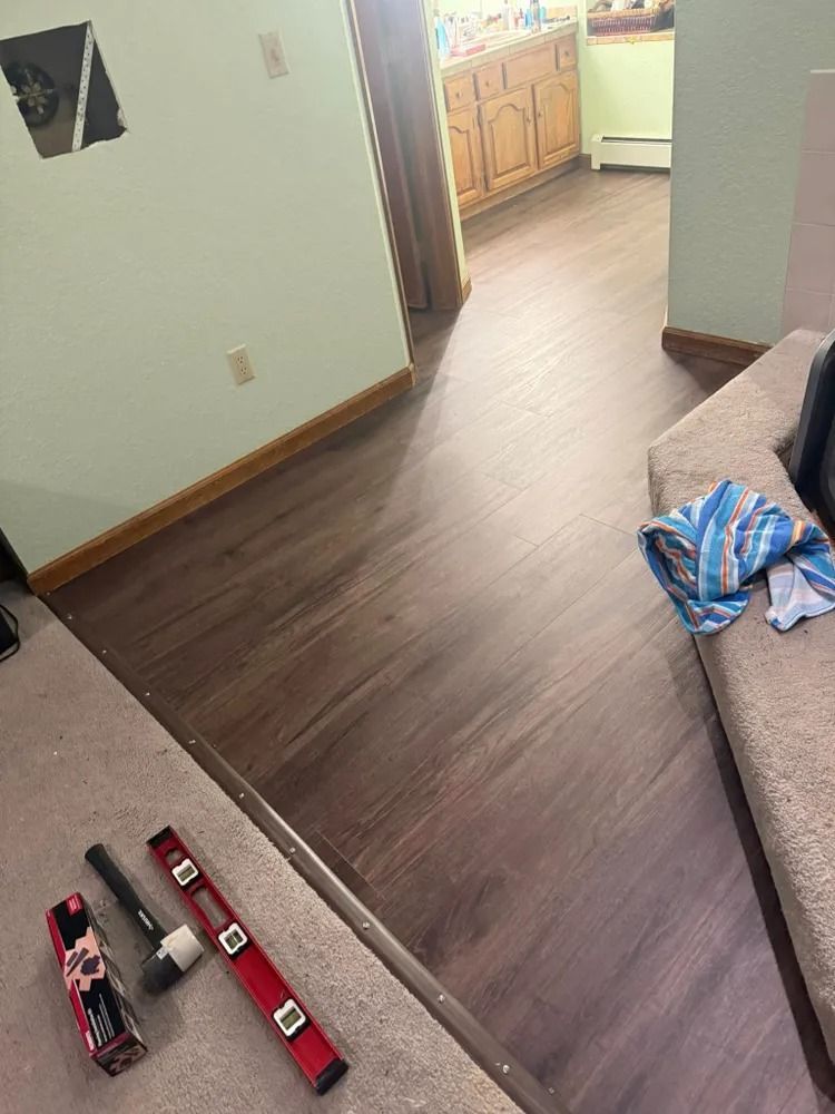 Living room with toy fire trucks on carpet and a blue-striped bag on a couch, looking toward a kitchen.
