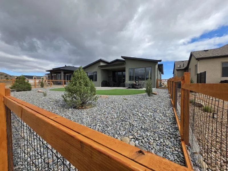 Modern house with gravel front yard and wooden fence under a cloudy sky