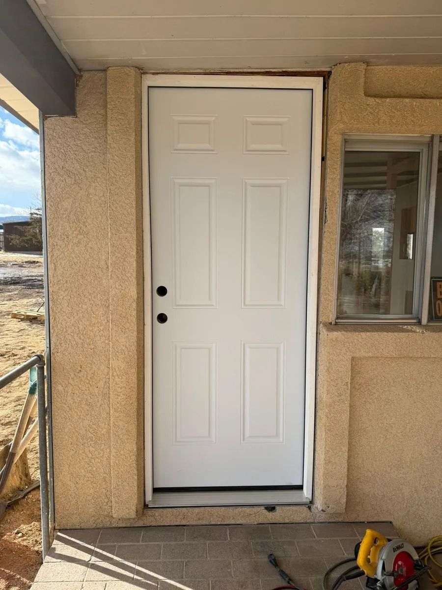 White front door with black handle on a stucco house exterior, beside a window and porch area