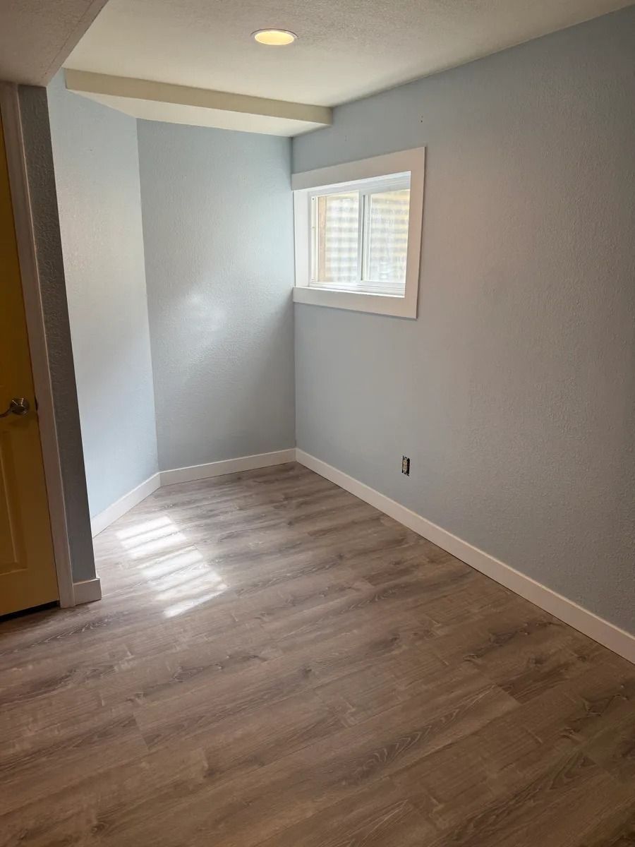 Empty light gray room with wood-look floors, a small window, and sunlight on the floor