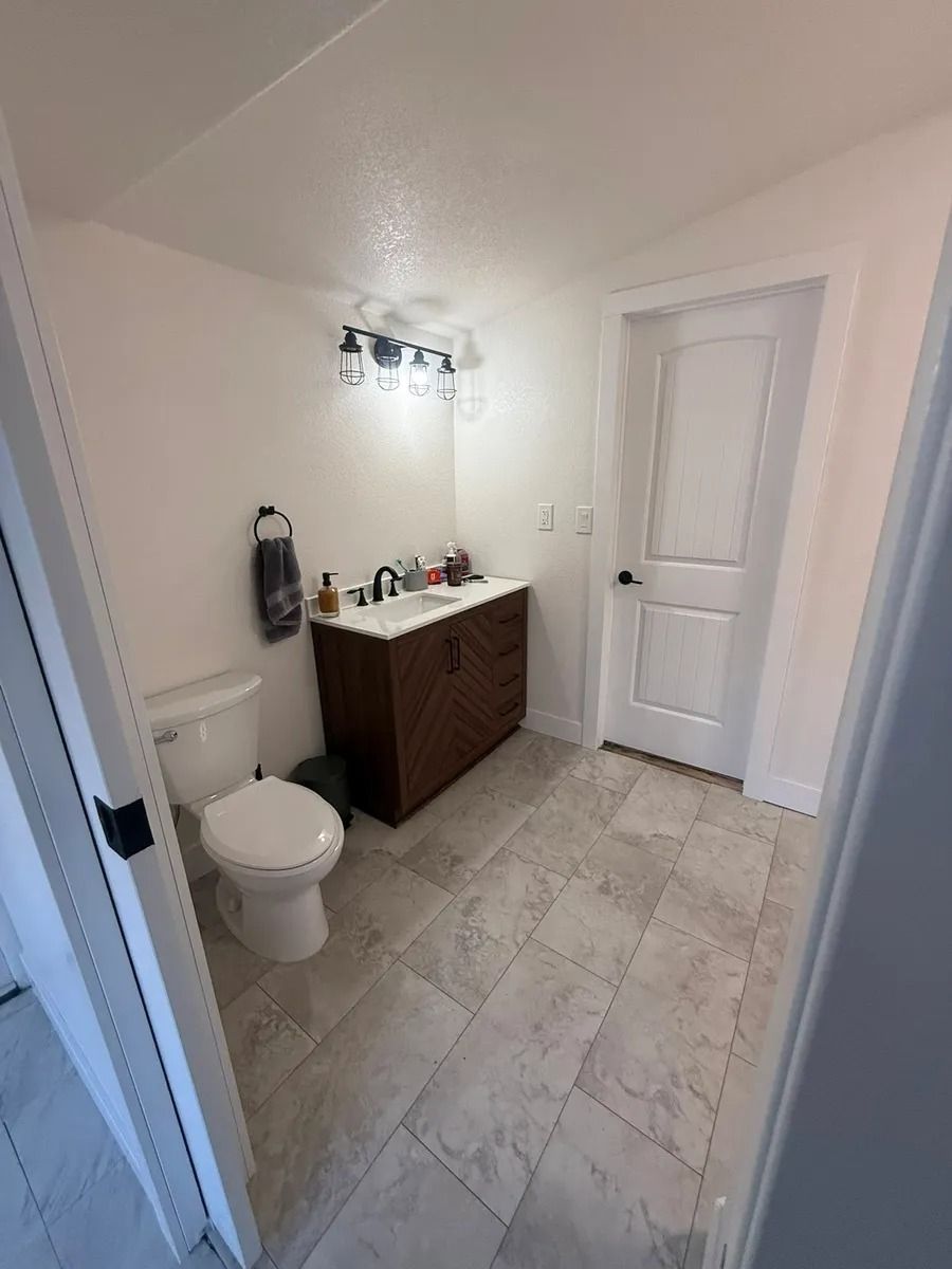 Small bathroom with toilet, dark vanity, mirror light, white door, and light tile floor.