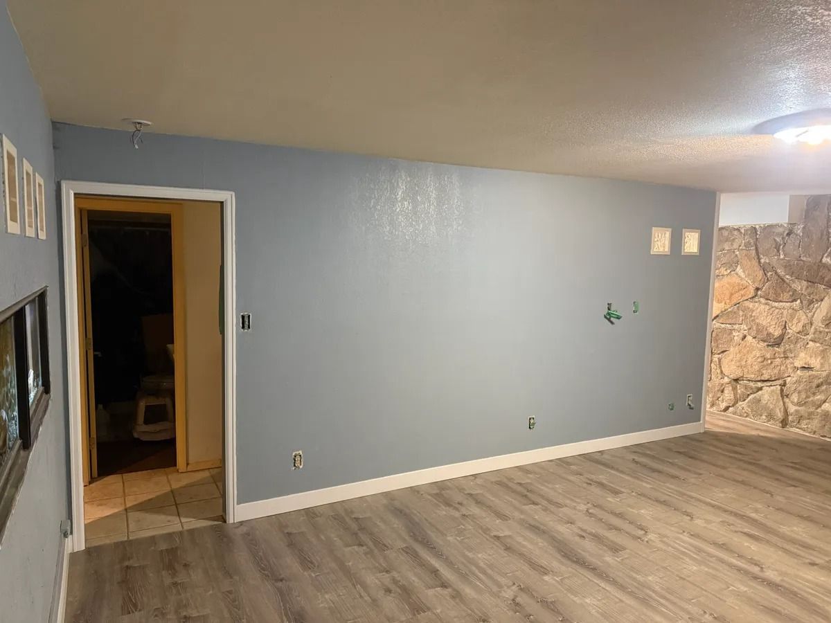 Empty living room with gray walls, wood flooring, open doorway, and stone accent wall.