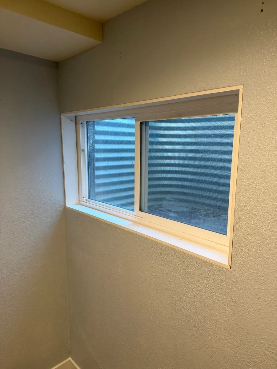 Small rectangular window with white trim in a beige room, showing blue striped exterior siding outside