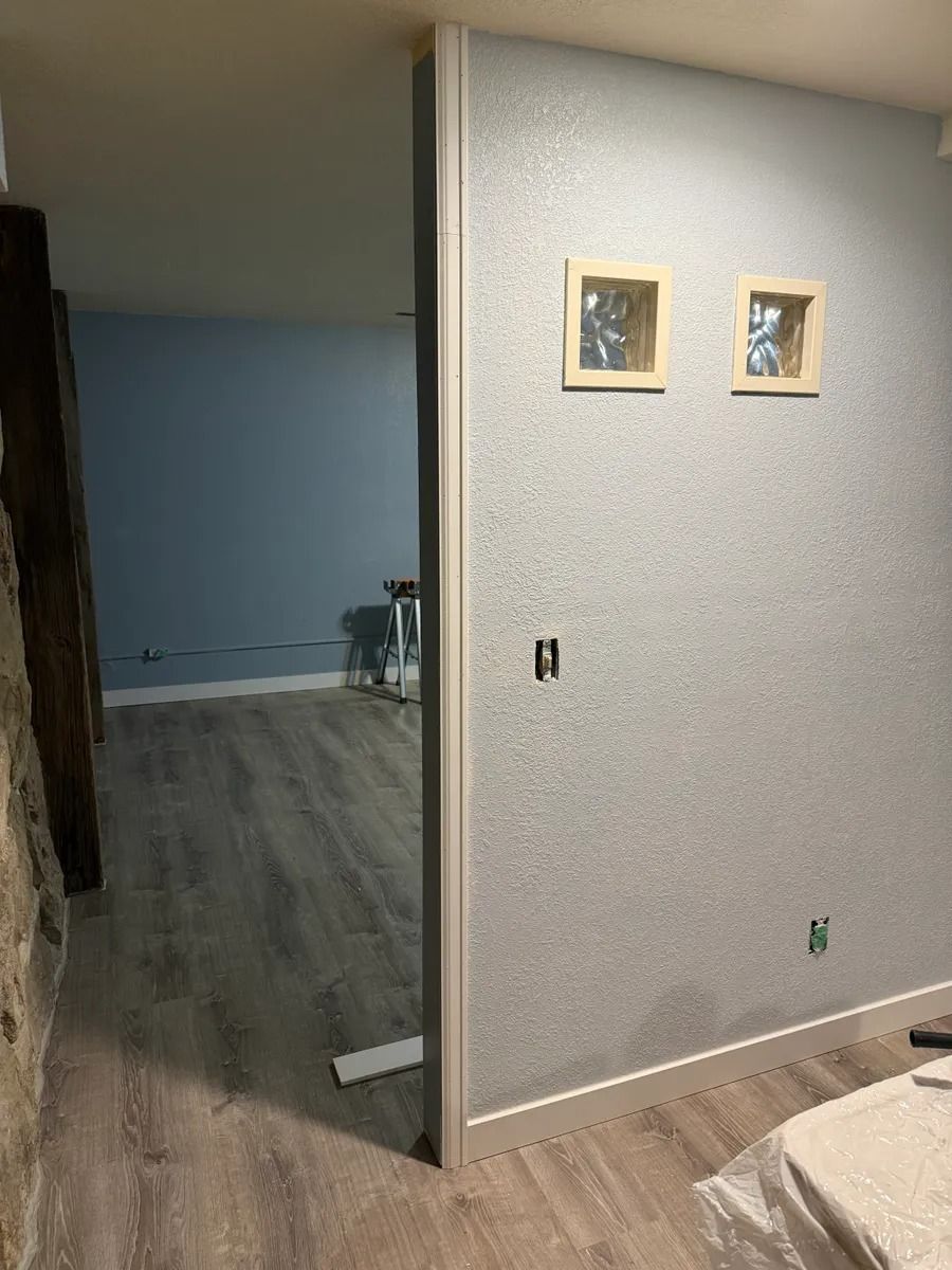 Partially renovated room with gray walls, wood floor, and two framed pictures on a partition wall