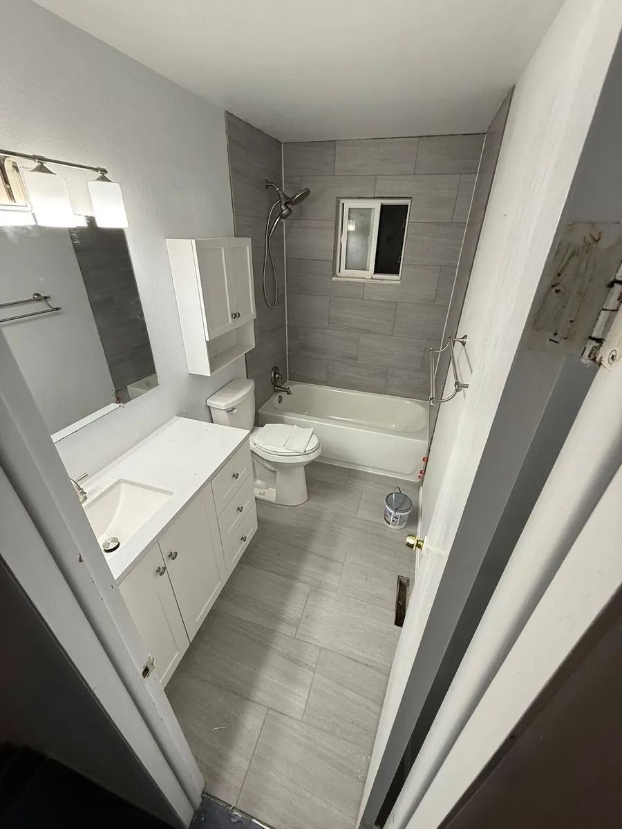 Modern gray-and-white bathroom with bathtub, toilet, vanity, and mirror seen through an open door