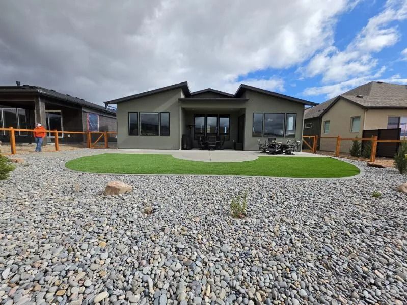 Modern single-story house with large windows, gravel front yard, and green lawn under a cloudy sky