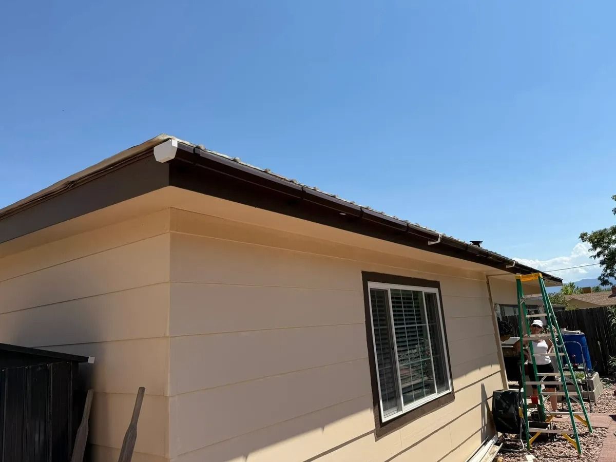 Tan house exterior with a window and sloped roof under a clear blue sky