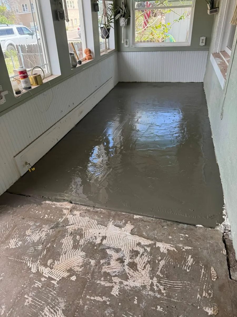 Freshly poured gray concrete floor in a narrow enclosed sunroom with windows on both sides.