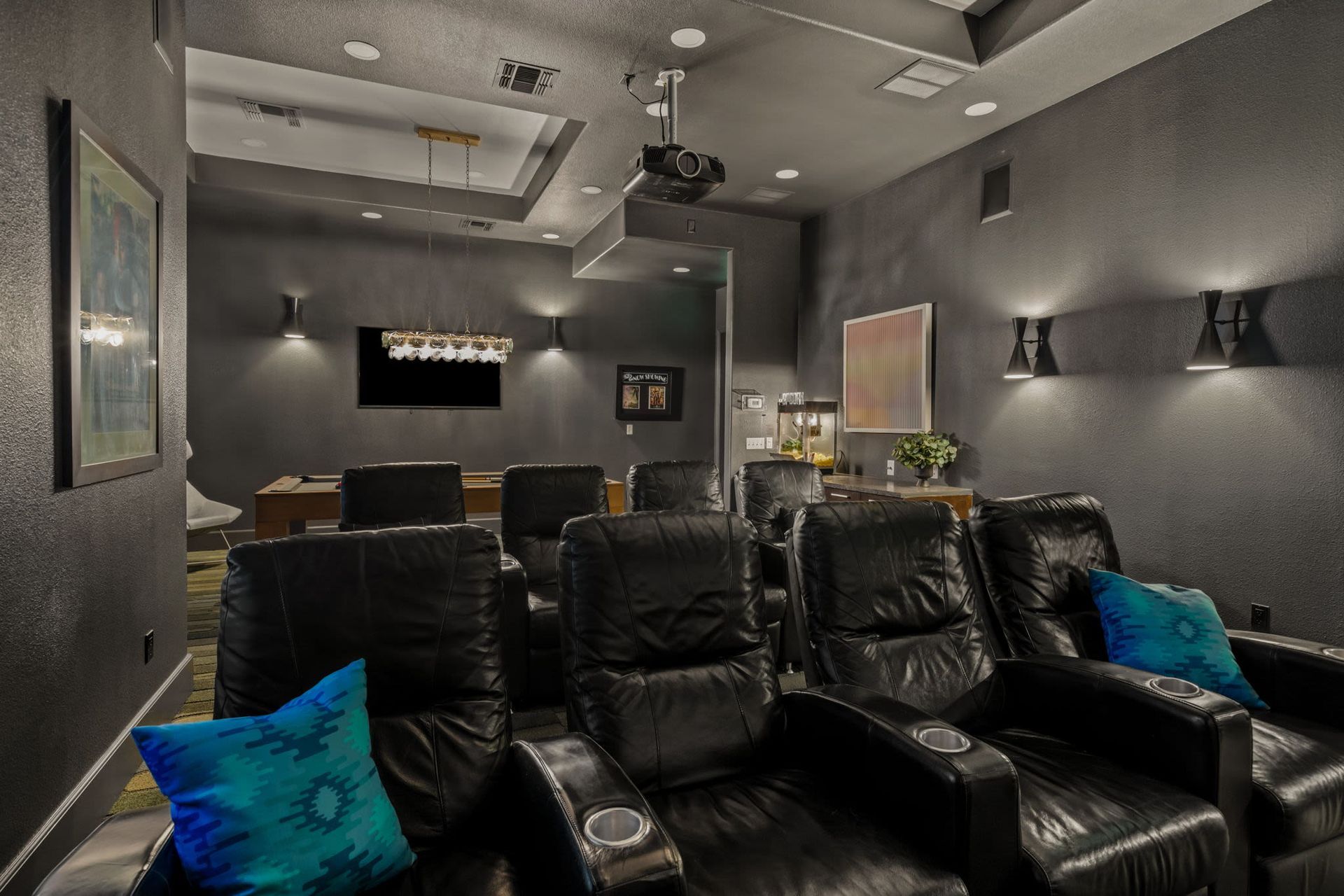 Dimly lit community media room with black leather recliners and a projector.