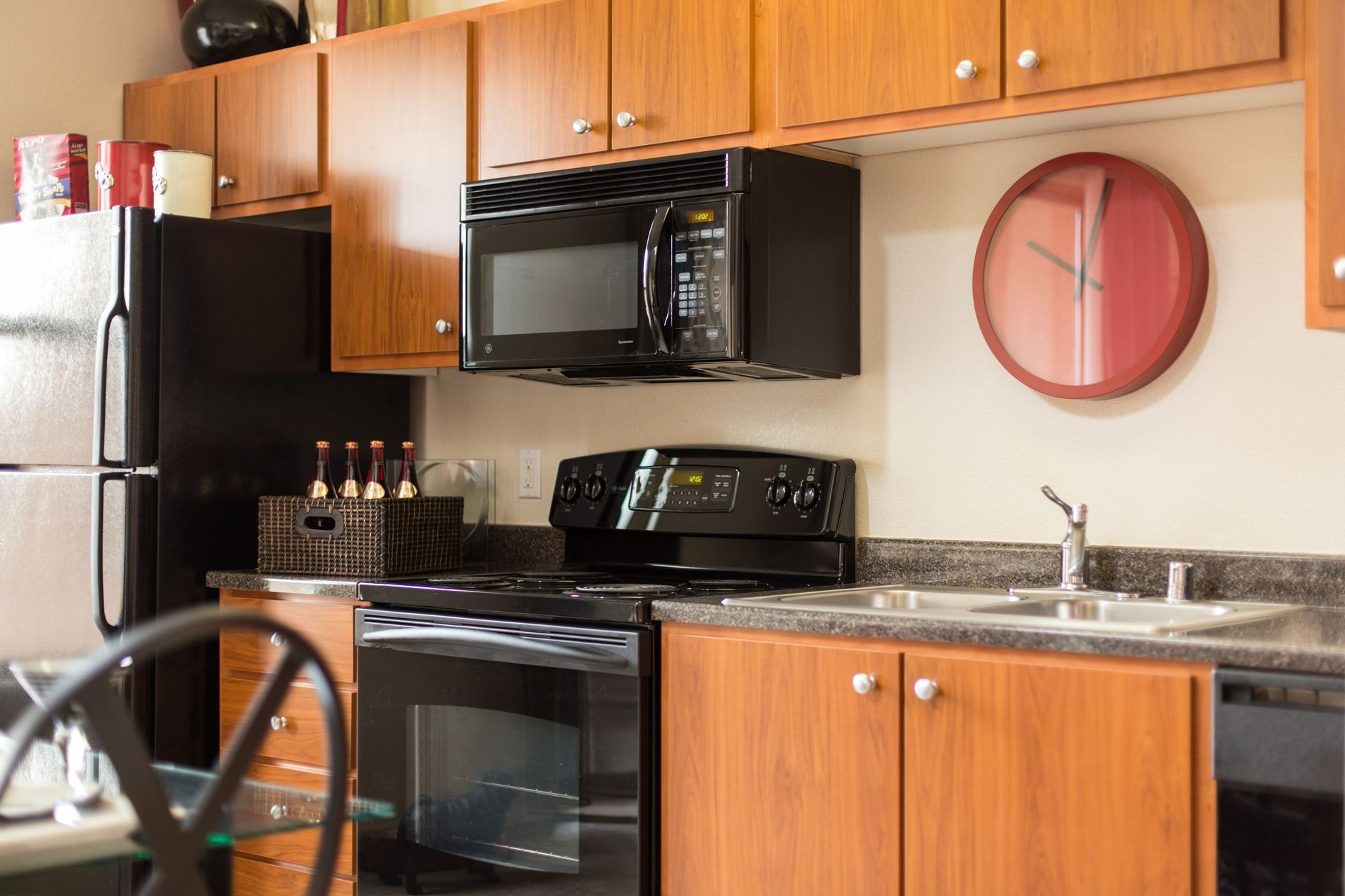 Kitchen in an apartment with black refrigerator, microwave, stove, and wooden cabinets.