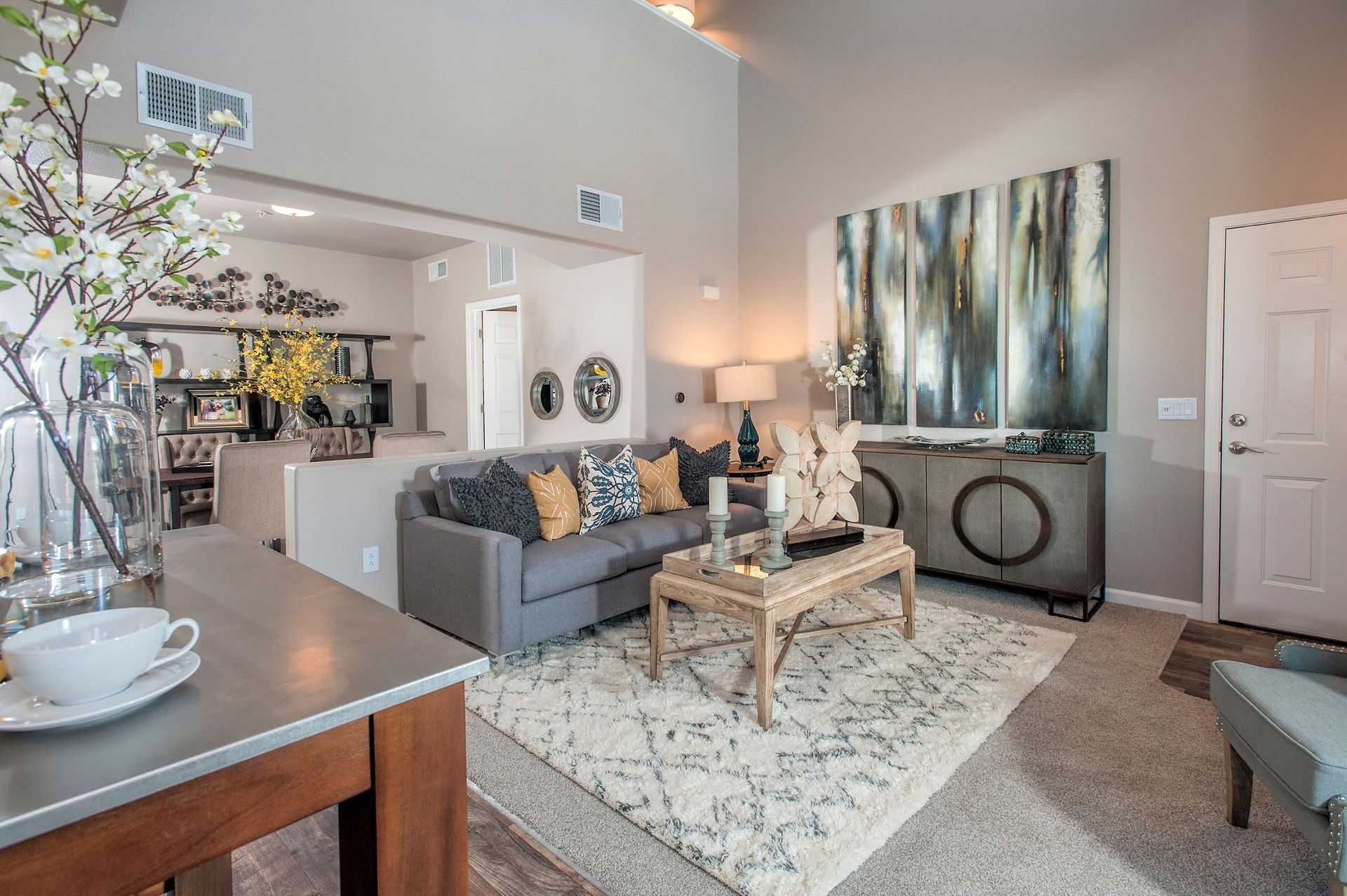 Living room in a modern apartment with a gray sofa, decorative pillows, and abstract wall art.