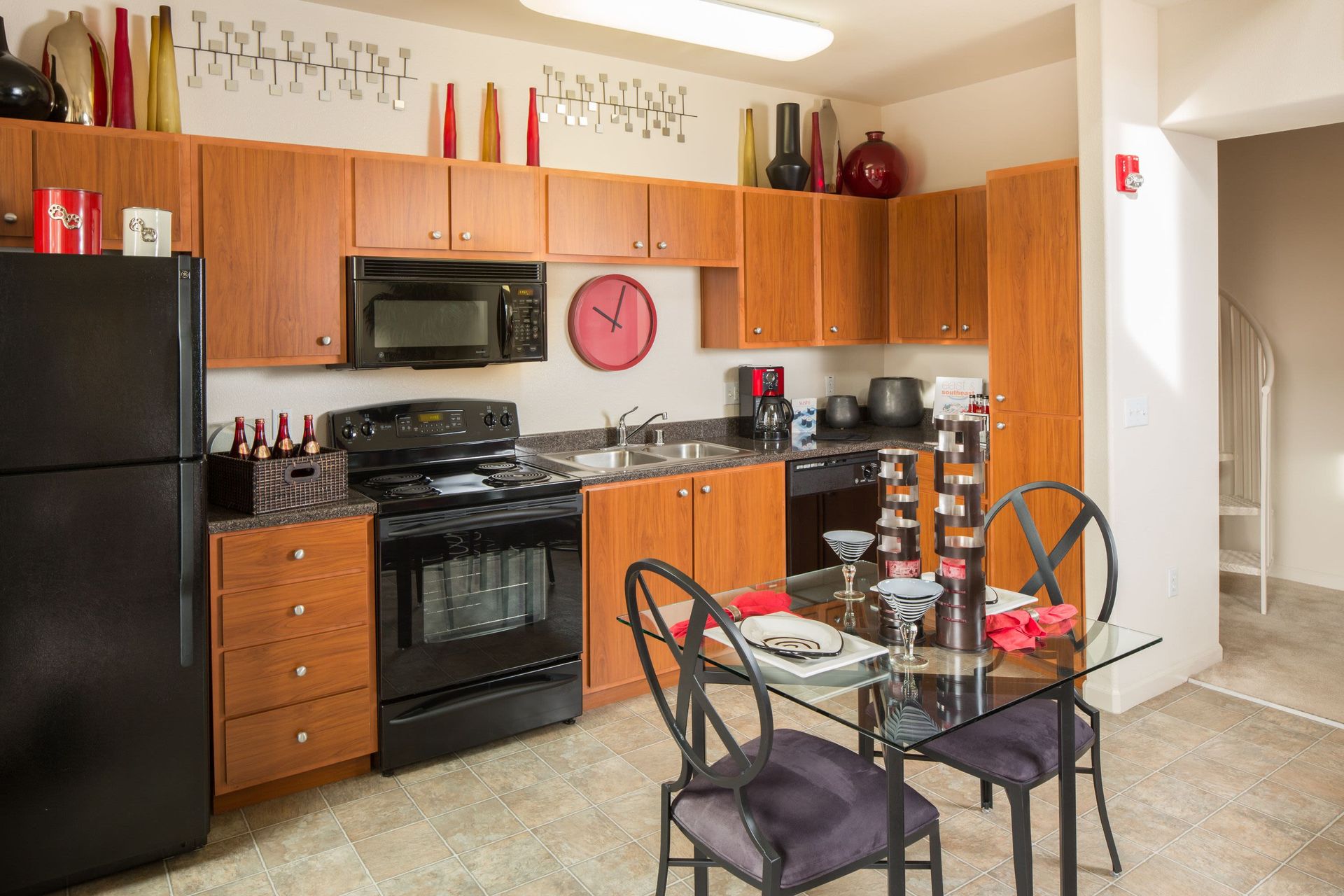 Kitchen in an apartment with wooden cabinets, black appliances, and a glass dining table.