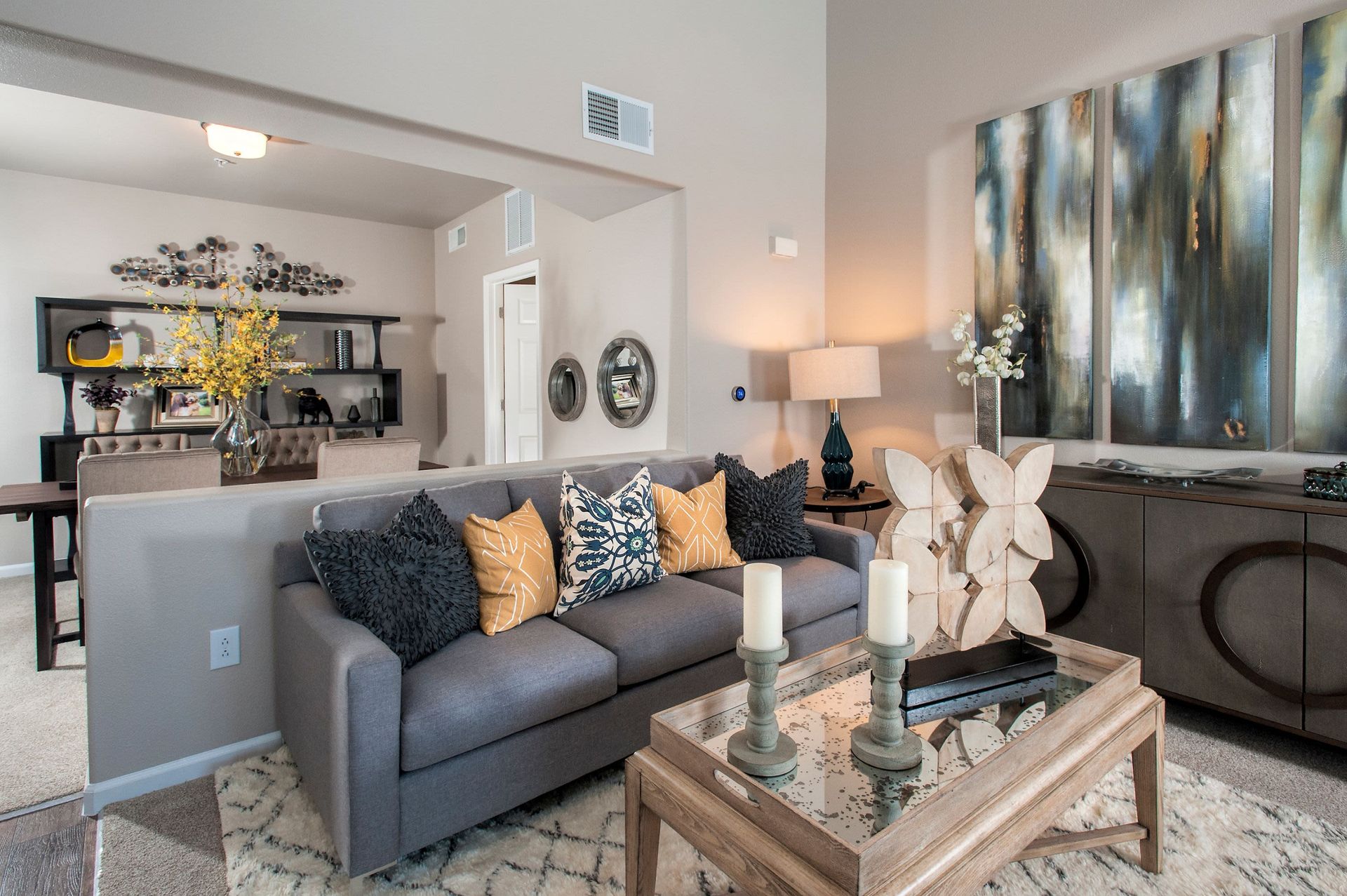Modern apartment living room with gray sofa, decor pillows, and a glass coffee table.