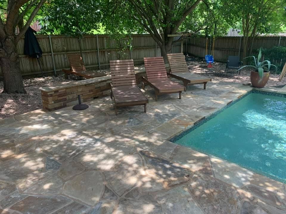 Poolside scene with stone patio, lounge chairs, fire pit, and fence.