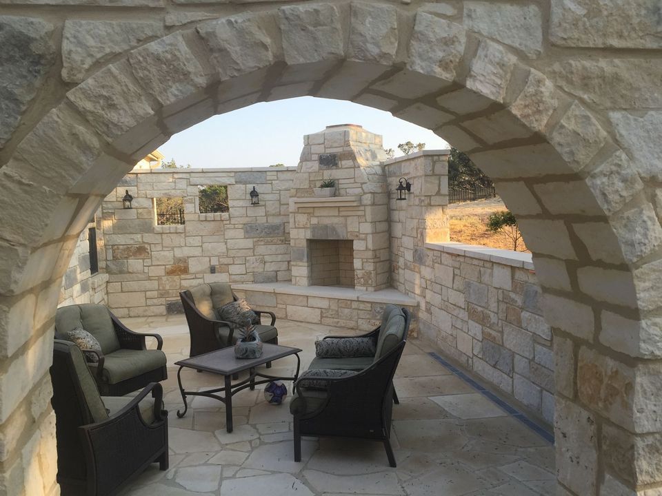 Stone patio with arched entry, seating area, fireplace, and surrounding walls.
