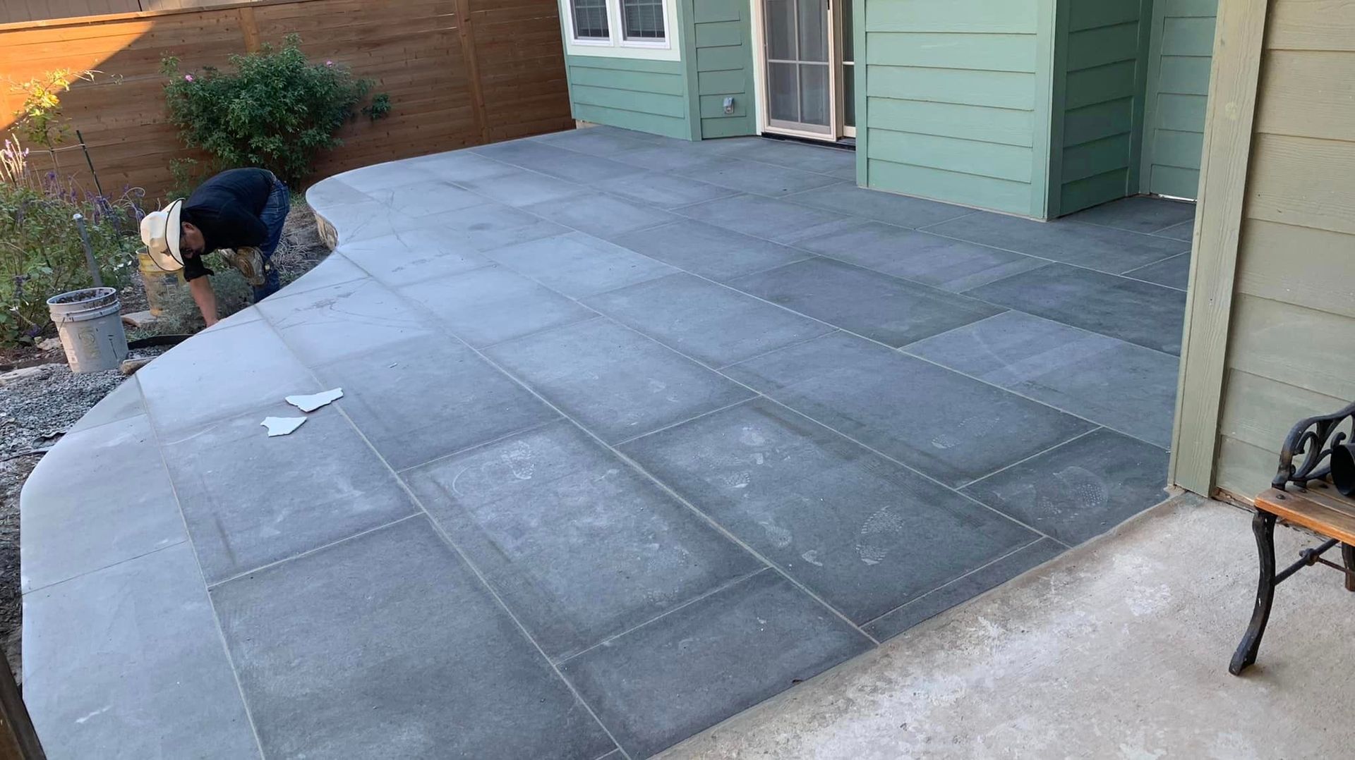 Man working on a newly paved gray patio, next to a green house.