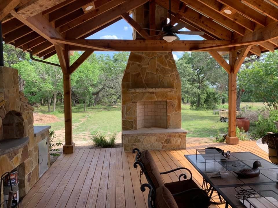 Wooden deck with stone fireplace and outdoor seating under a wooden pergola.