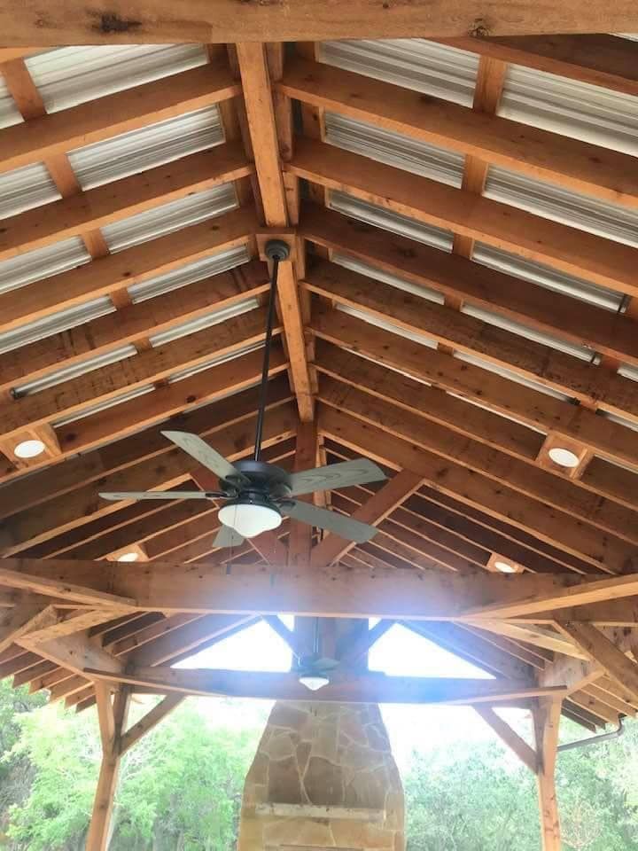 Wooden pavilion interior with ceiling fan and corrugated metal roof.