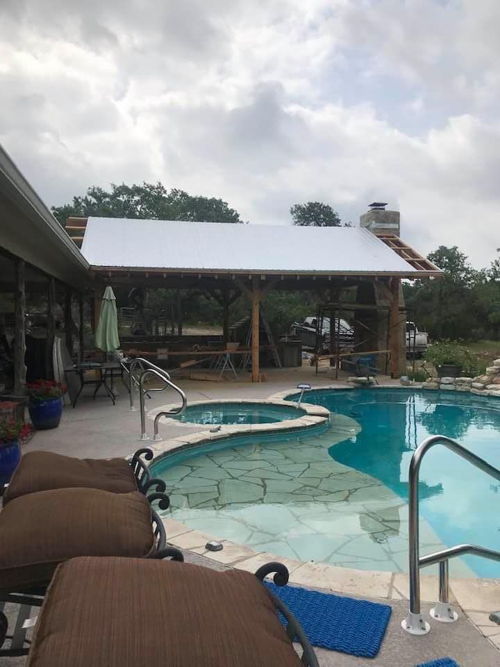 Poolside with a covered patio under construction, partially finished roof, spa, and lounge chairs.