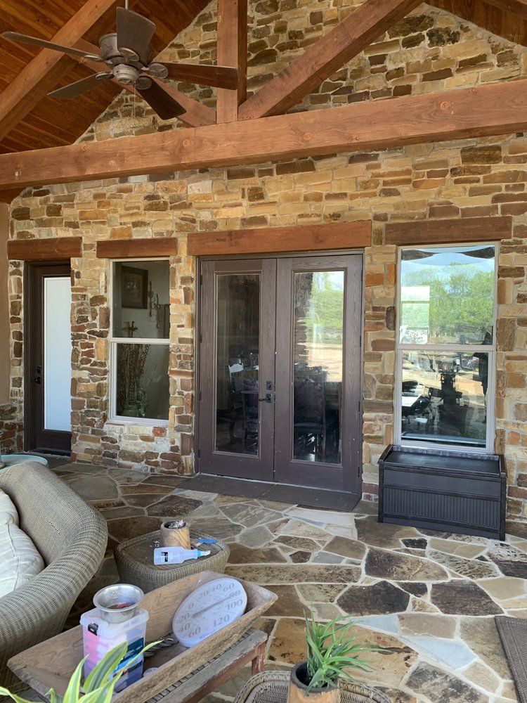 Outdoor patio with stone floor and brick wall, doors and windows with brown trim.