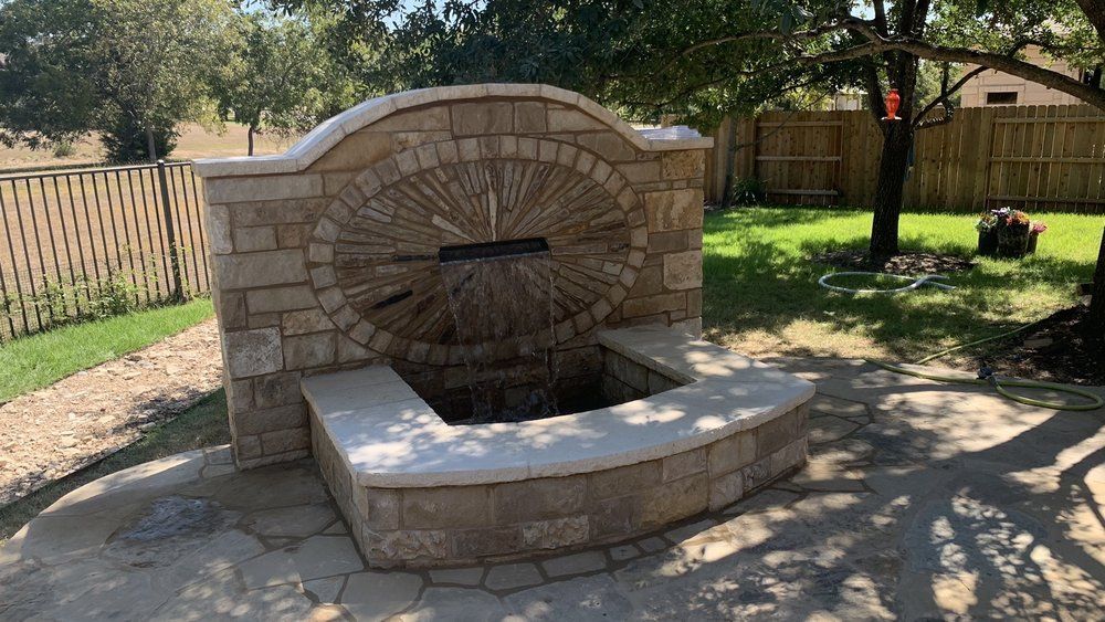 Stone water fountain in a backyard setting, with water cascading into a curved basin.