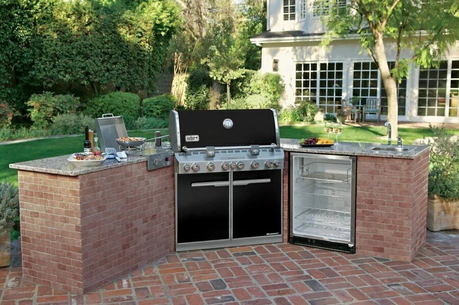 Outdoor kitchen with brick surround, built-in grill, and refrigerator.