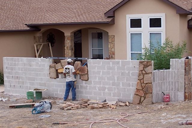 Covered patio with stone fireplace, TV, and fan. Outdoor seating and firewood storage.