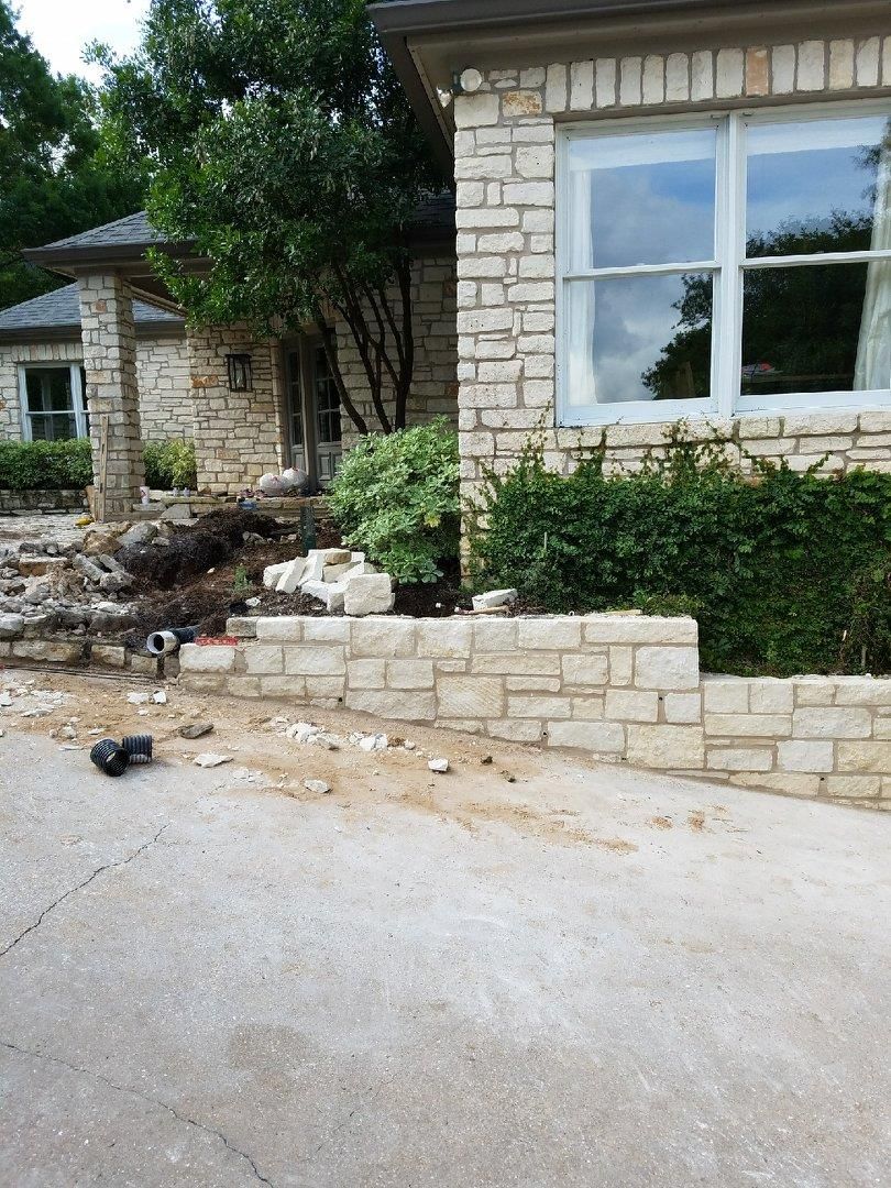 Stone wall with three arched windows; trees and a building are visible behind it.
