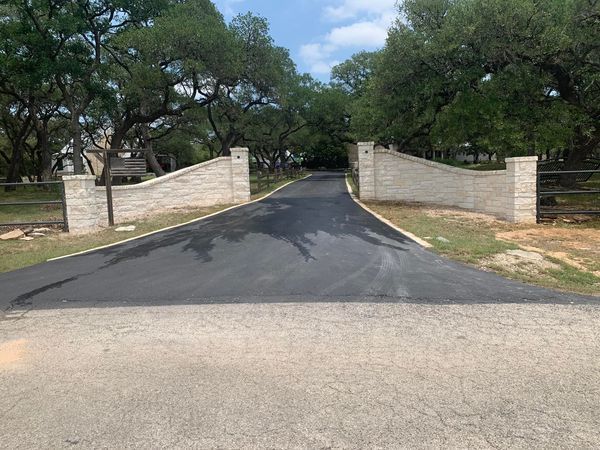 Stone retaining walls border a gravel path leading into a garden with trees and a building in the background.