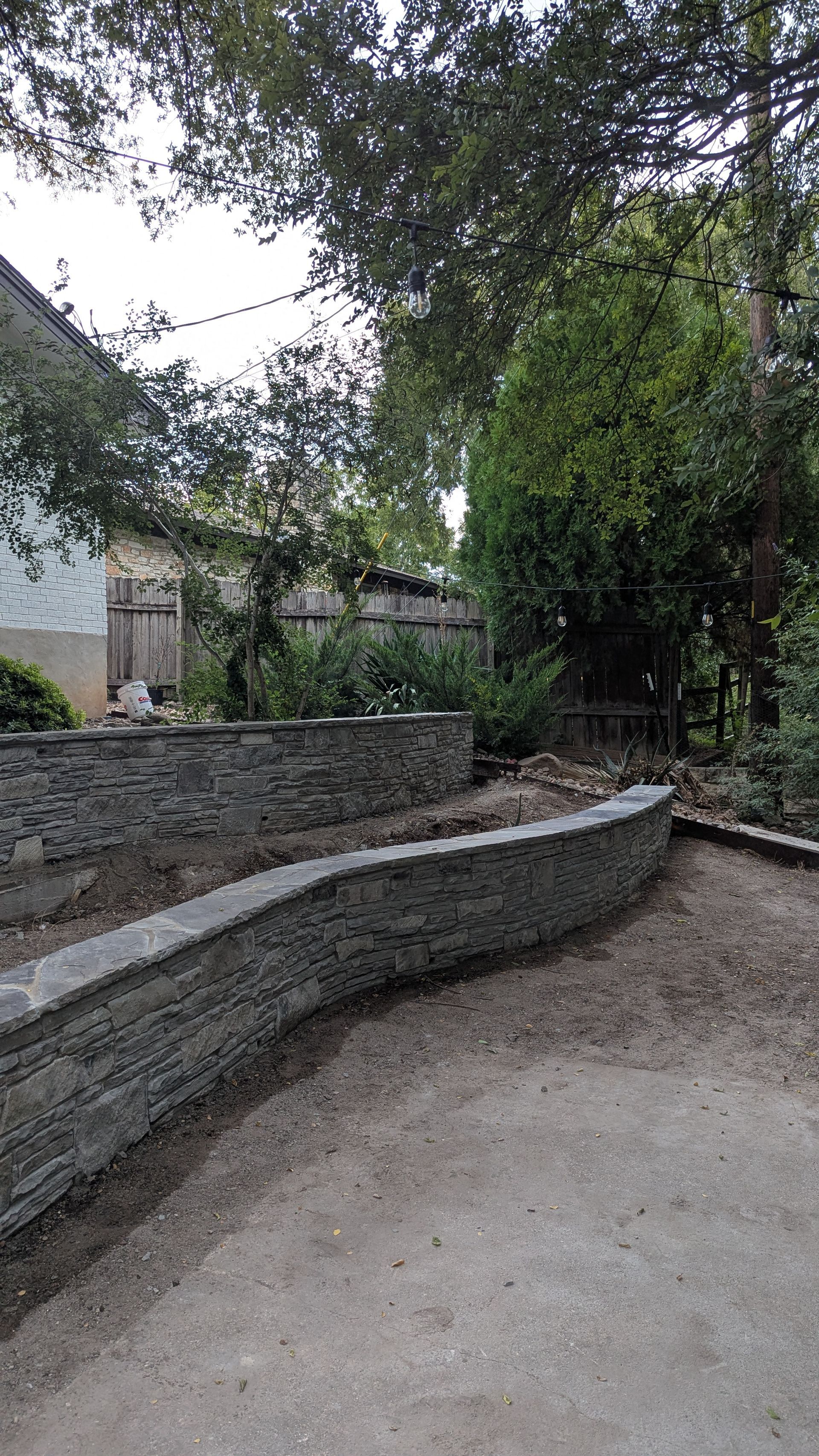 Stone retaining walls border a gravel path leading into a garden with trees and a building in the background.