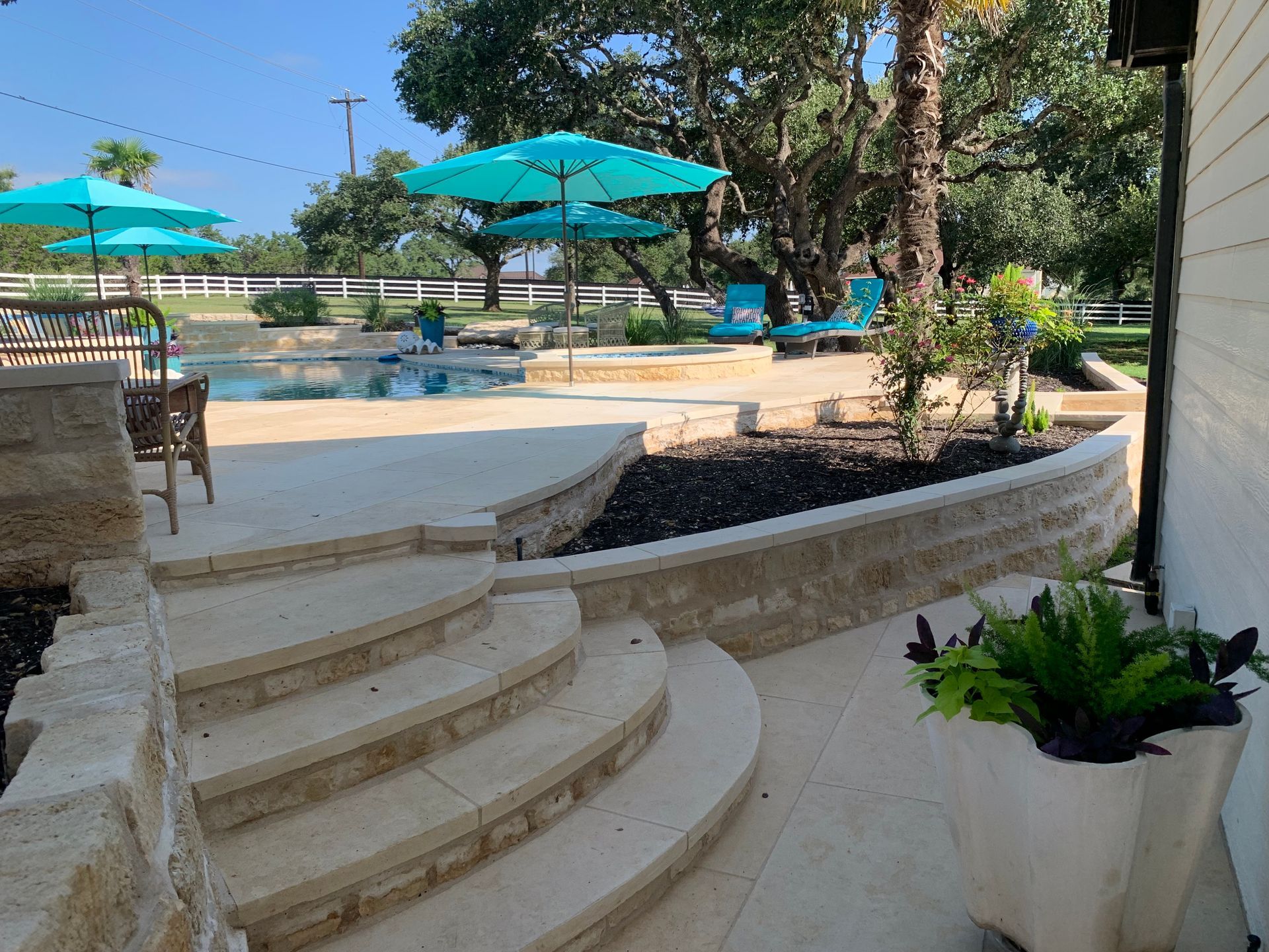 Stone steps leading to a backyard pool area with blue umbrellas, lounge chairs, and landscaping.