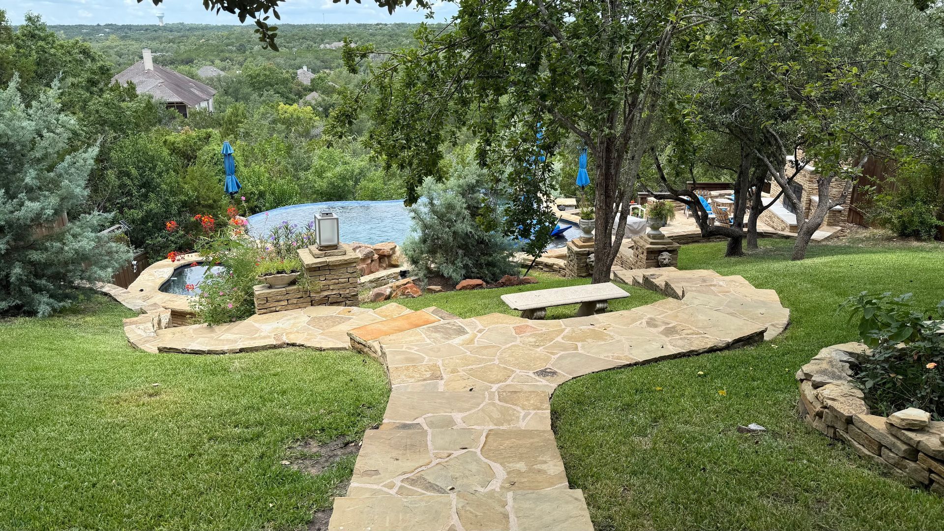Stone pathway through a garden with a pool and greenery.