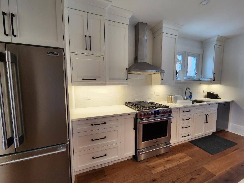 White kitchen with stainless steel appliances, cabinets, and range hood; hardwood floors.