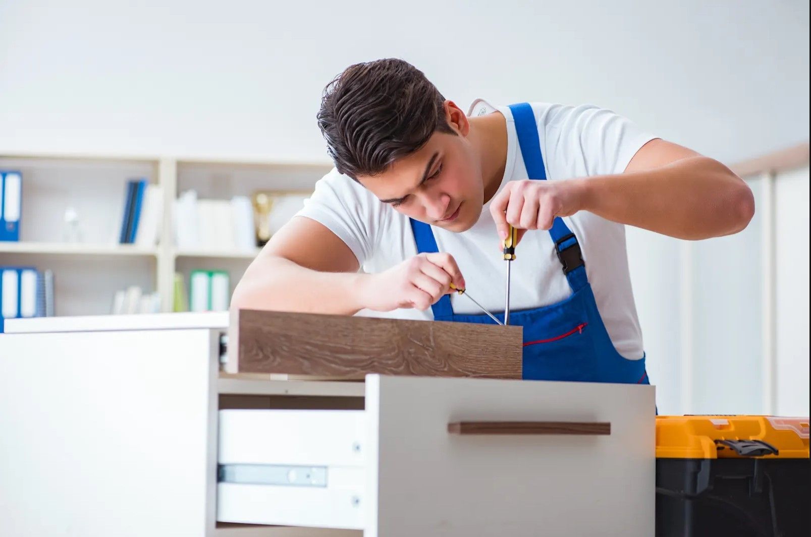 A man is working on a cabinet with a screwdriver.