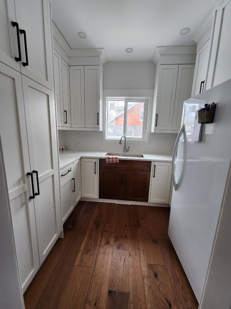 White kitchen with dark wood cabinets, sink, and appliances; white countertops and cabinetry.