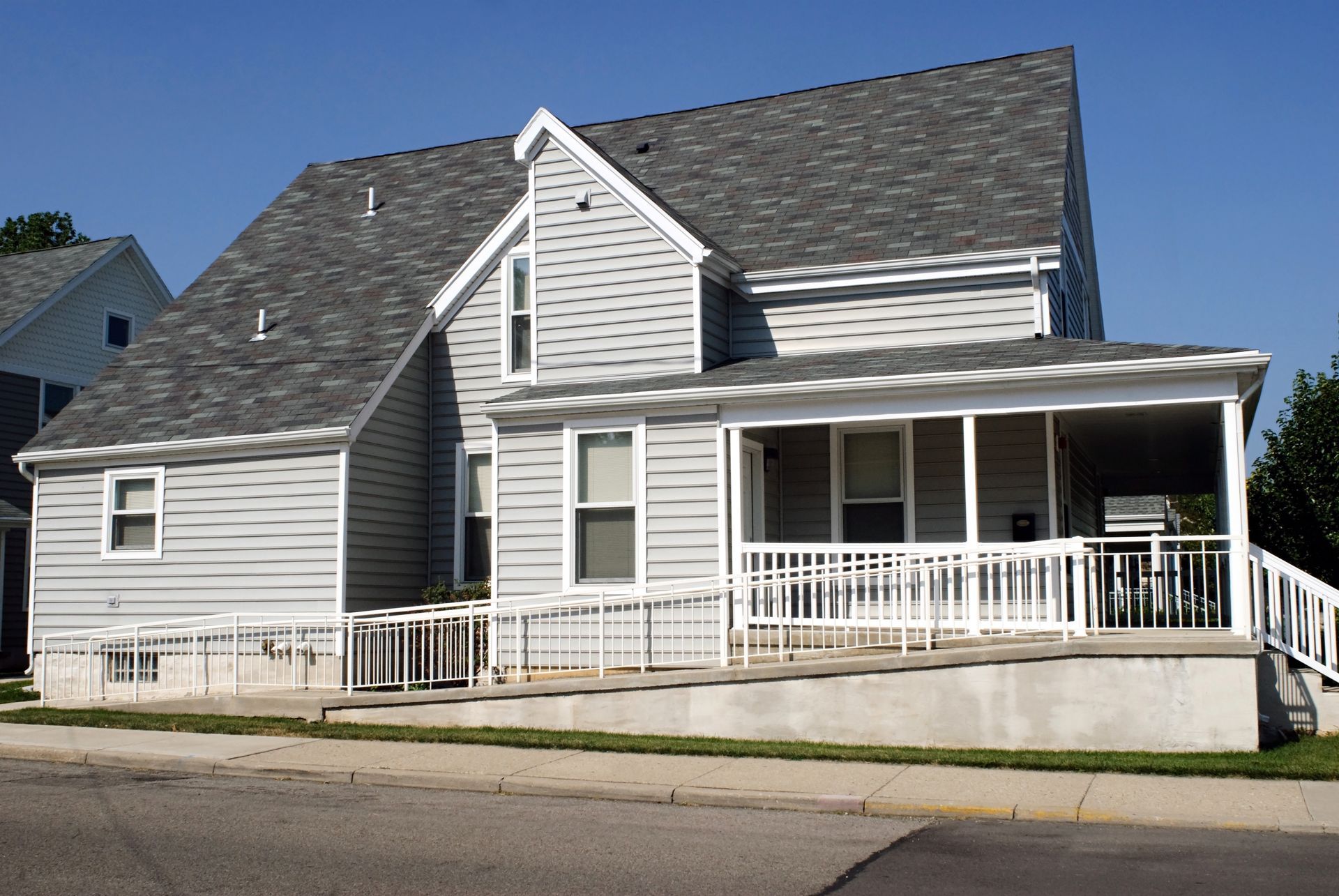Two-story house with gray siding, porch, and a wheelchair ramp.