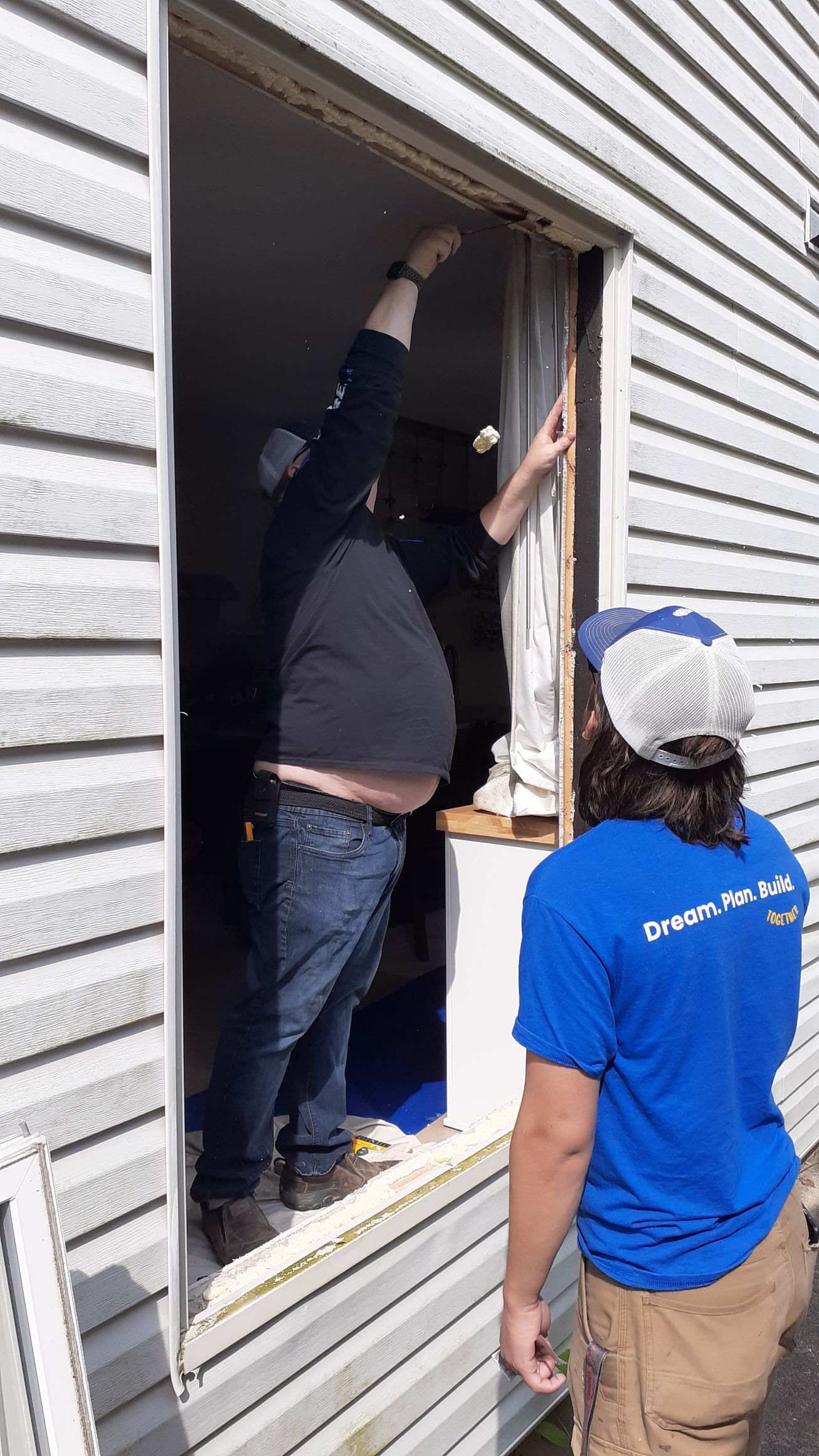 Two men are working on a window on a house.
