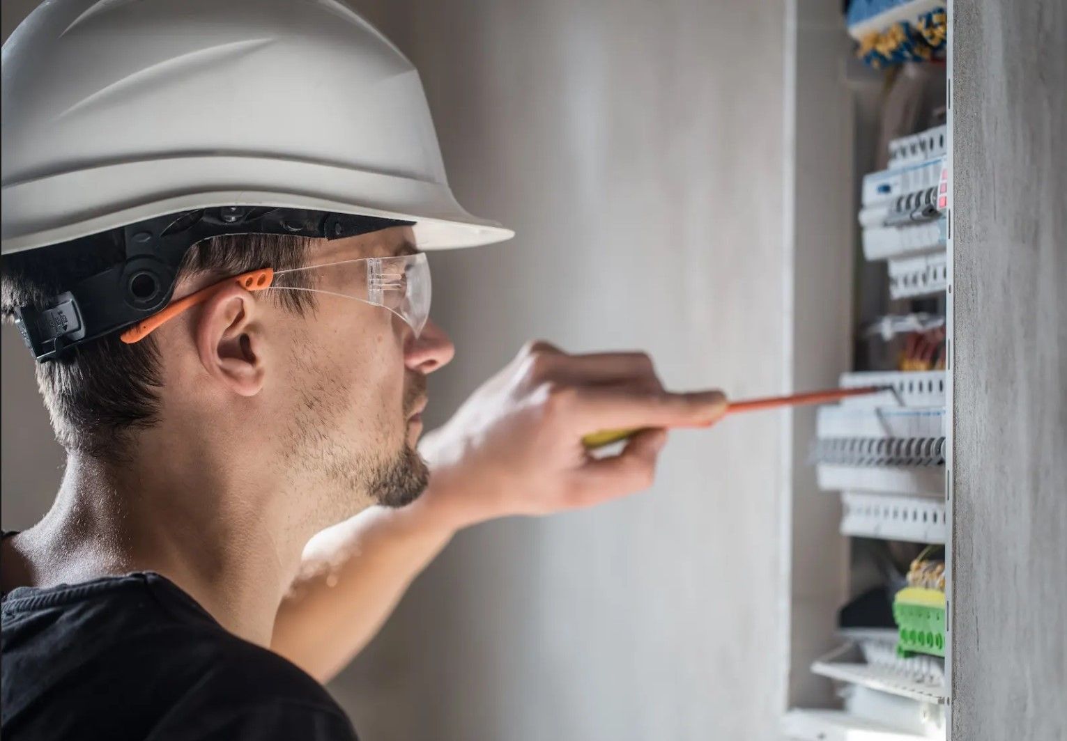 A man wearing a hard hat and safety glasses is working on an electrical box.