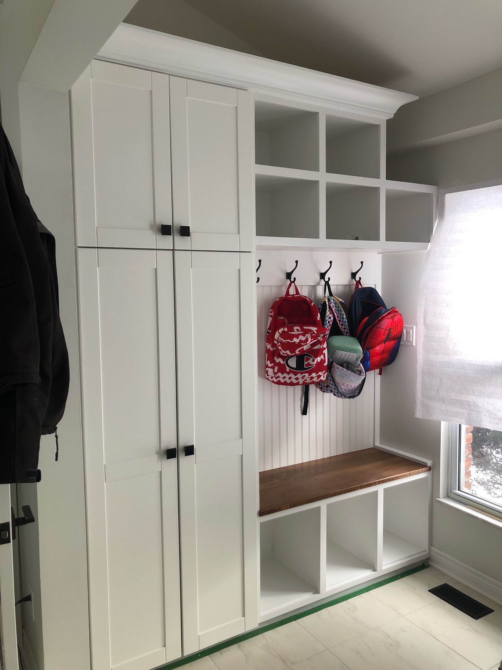 A room with white cabinets and backpacks hanging on hooks