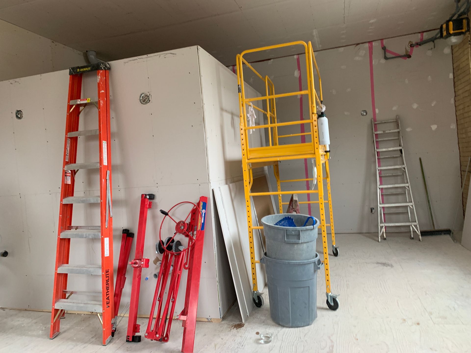 A room with a ladder , scaffolding , and a trash can.