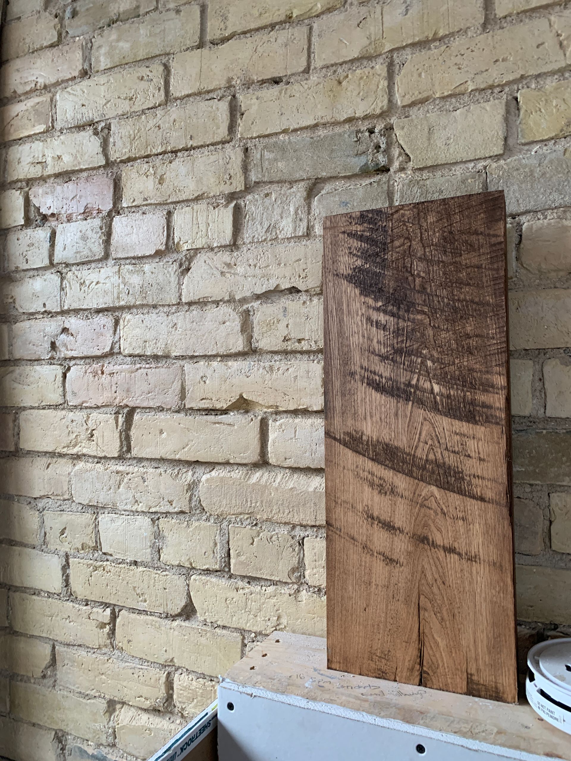 A wooden cutting board is sitting on a shelf in front of a brick wall.