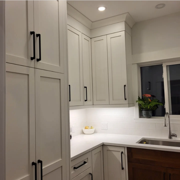 A kitchen with white cabinets and black handles