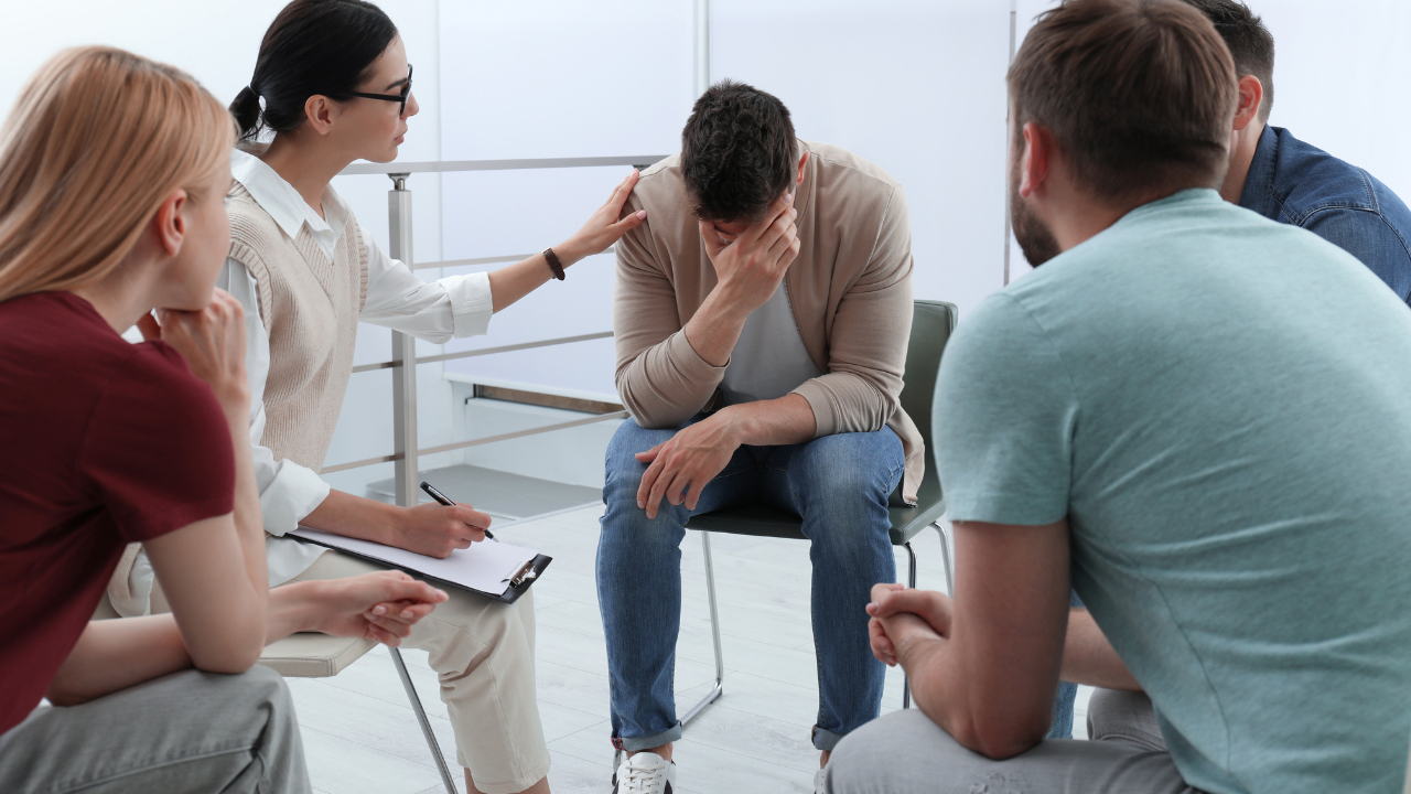 A group of people are sitting in a circle with a man sitting in the middle.