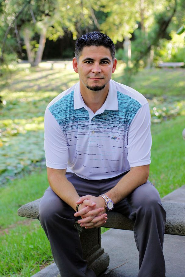 A man is sitting on a bench in a park with his hands folded.