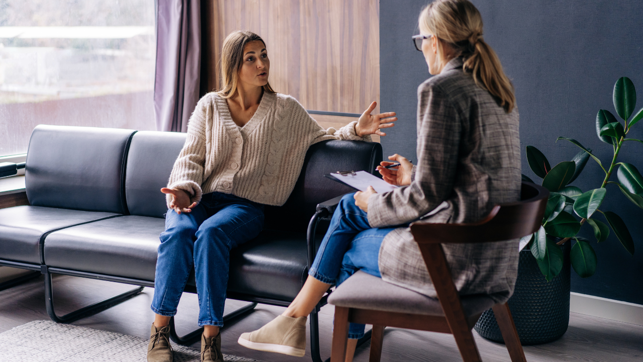 Two women are sitting on a couch talking to each other.