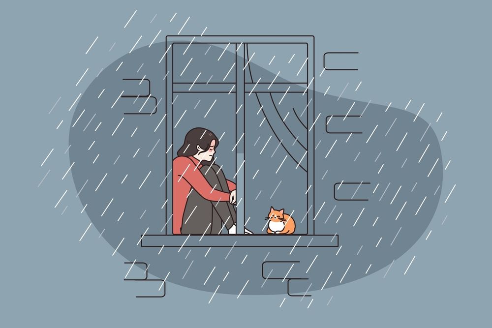 A woman is sitting on a window sill in the rain with her cat.