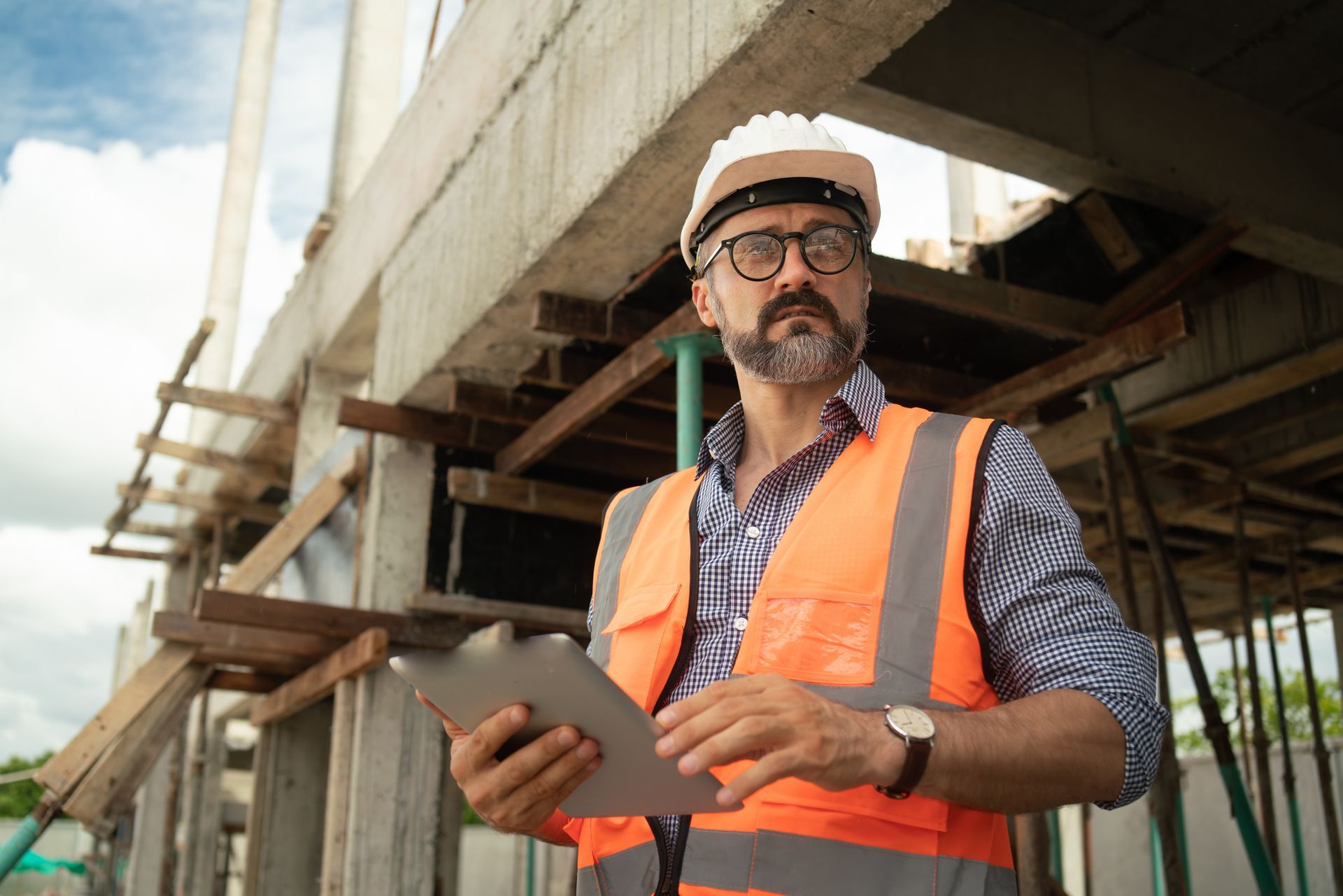 A construction worker is standing in front of a building holding a tablet.