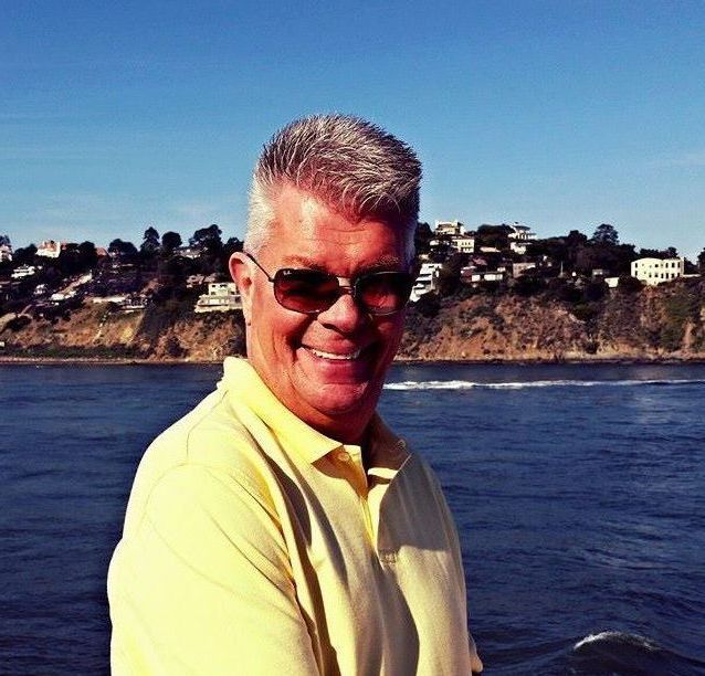 A man wearing sunglasses and a yellow shirt stands in front of a body of water