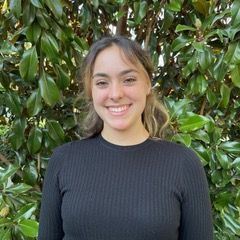 A man wearing sunglasses and a yellow shirt stands in front of a body of water