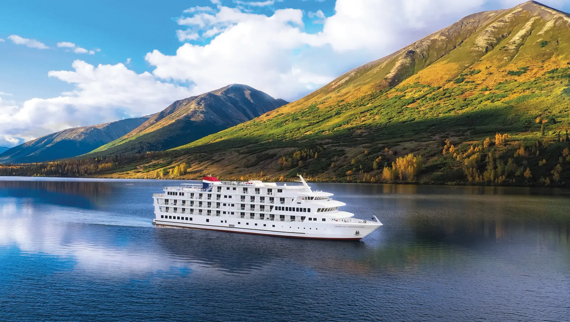 A cruise ship is floating on top of a lake with mountains in the background.